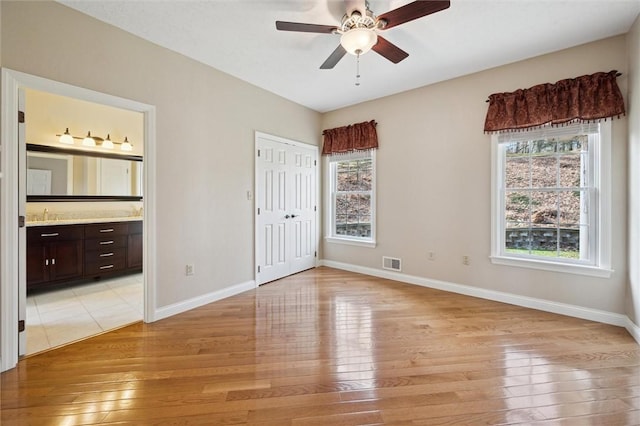 unfurnished bedroom with ceiling fan, connected bathroom, light wood-type flooring, and a closet