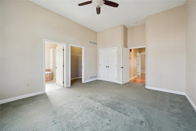 unfurnished bedroom with ceiling fan, a high ceiling, carpet, connected bathroom, and multiple closets