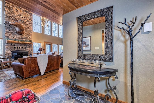 living room with a high ceiling, a notable chandelier, wood-type flooring, a stone fireplace, and wooden ceiling