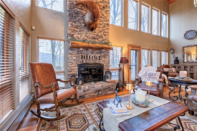 living room with hardwood / wood-style floors, a stone fireplace, a baseboard radiator, and a high ceiling