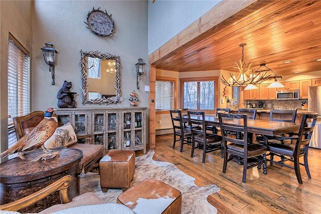 dining room with a baseboard heating unit, a chandelier, light hardwood / wood-style floors, and wooden ceiling