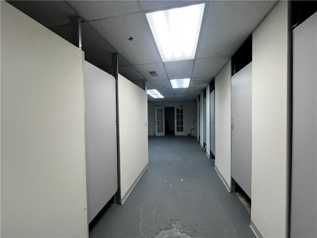 hallway with a paneled ceiling and concrete floors