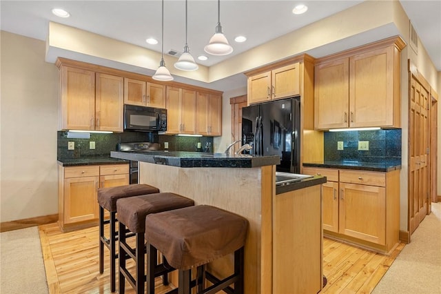 kitchen featuring pendant lighting, a kitchen bar, black appliances, a center island with sink, and light brown cabinets