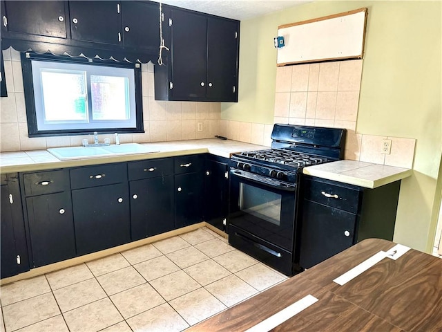 kitchen featuring light tile patterned floors, black range with gas stovetop, sink, and backsplash