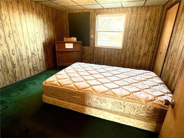 bedroom featuring a drop ceiling, dark carpet, and wood walls