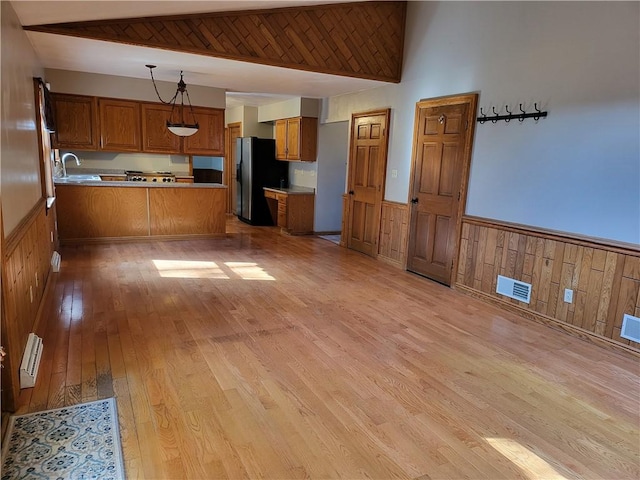 kitchen with sink, light hardwood / wood-style flooring, stainless steel refrigerator with ice dispenser, decorative light fixtures, and kitchen peninsula