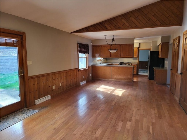 kitchen featuring pendant lighting, lofted ceiling, stainless steel fridge, kitchen peninsula, and light wood-type flooring