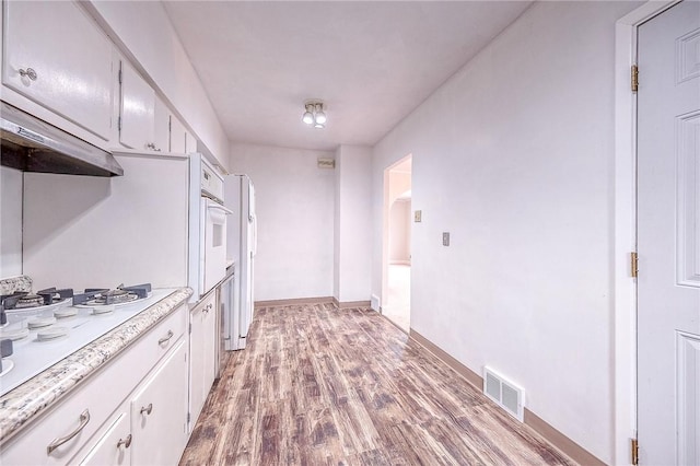 kitchen with white appliances, exhaust hood, light hardwood / wood-style flooring, and white cabinets