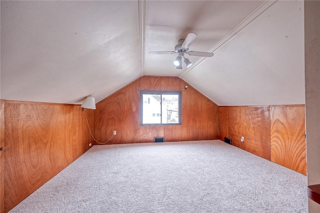 bonus room featuring lofted ceiling, wooden walls, ceiling fan, and carpet