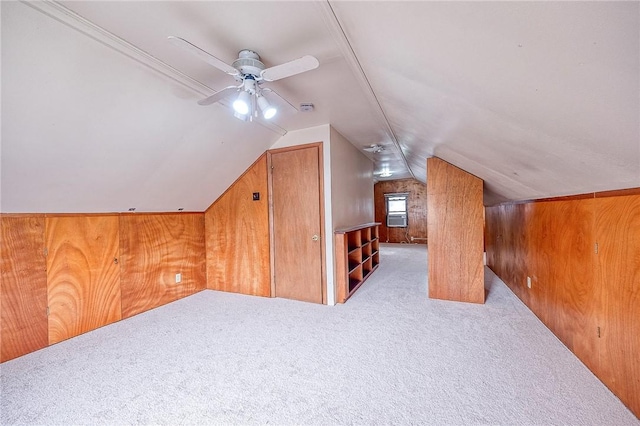 additional living space with ceiling fan, vaulted ceiling, light carpet, and wood walls