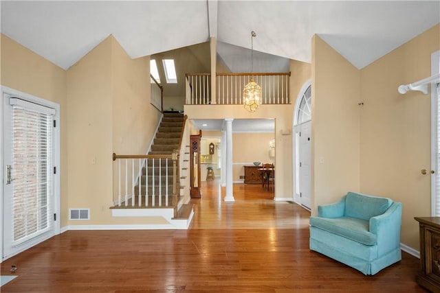 entryway with decorative columns, wood-type flooring, a notable chandelier, and high vaulted ceiling