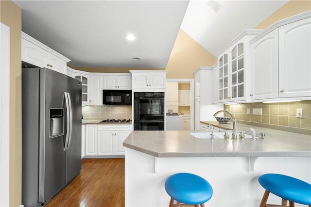 kitchen with washing machine and dryer, black appliances, white cabinets, a kitchen bar, and kitchen peninsula