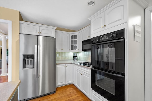 kitchen featuring light hardwood / wood-style flooring, black appliances, white cabinets, decorative backsplash, and ornate columns