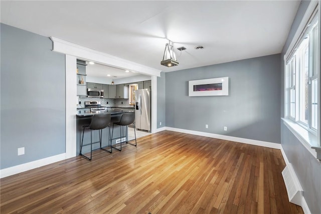 kitchen featuring hardwood / wood-style floors, decorative backsplash, gray cabinets, and appliances with stainless steel finishes