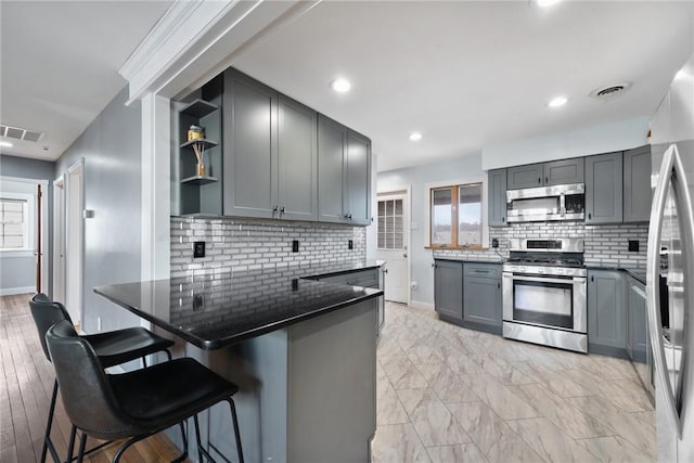 kitchen featuring stainless steel appliances, gray cabinetry, a breakfast bar area, and kitchen peninsula