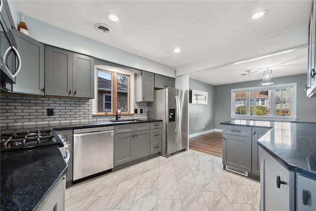 kitchen featuring sink, gray cabinets, appliances with stainless steel finishes, tasteful backsplash, and dark stone counters