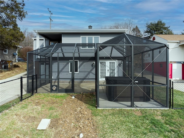 rear view of house featuring a lawn, glass enclosure, and french doors