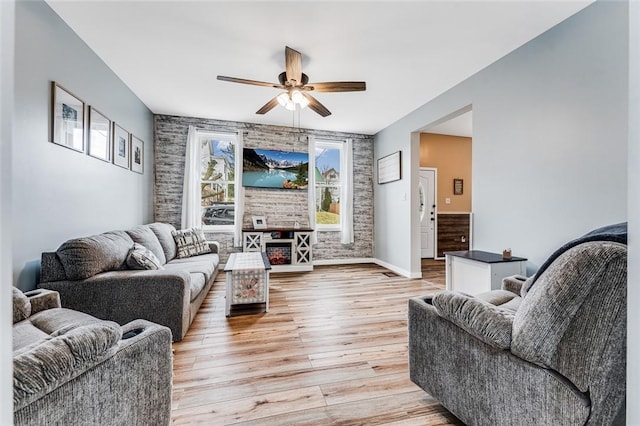 living room featuring ceiling fan, brick wall, and light wood-type flooring