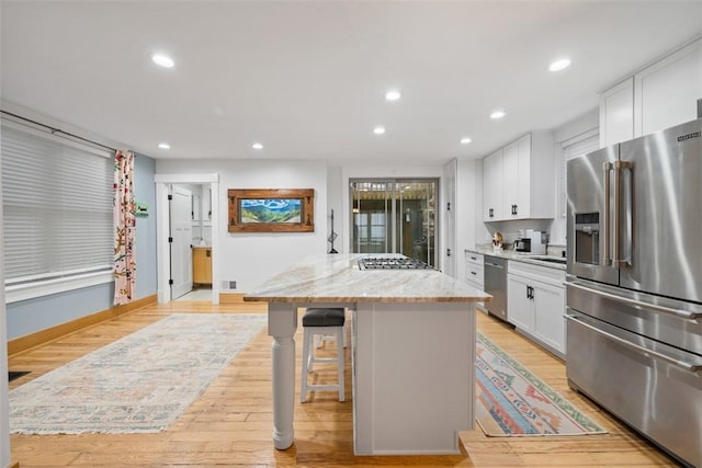 kitchen with light stone counters, stainless steel appliances, a center island, and white cabinets