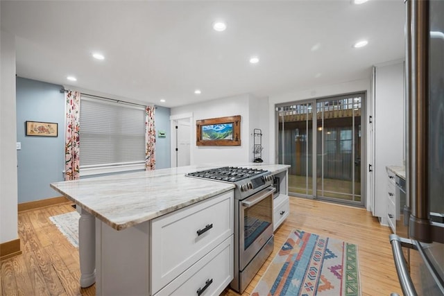 kitchen featuring light wood-type flooring, white cabinetry, stainless steel gas range, and a kitchen island