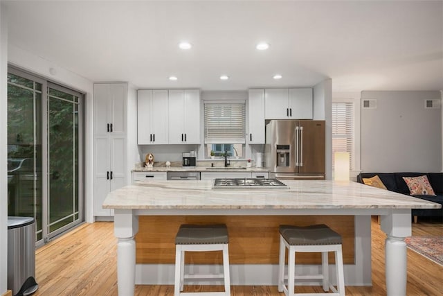 kitchen featuring sink, a breakfast bar, appliances with stainless steel finishes, white cabinetry, and light stone counters