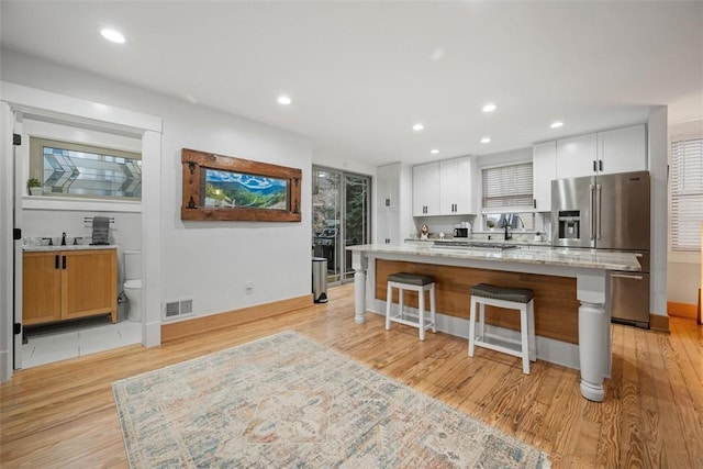 kitchen featuring a kitchen island, high quality fridge, a breakfast bar area, white cabinets, and light stone countertops