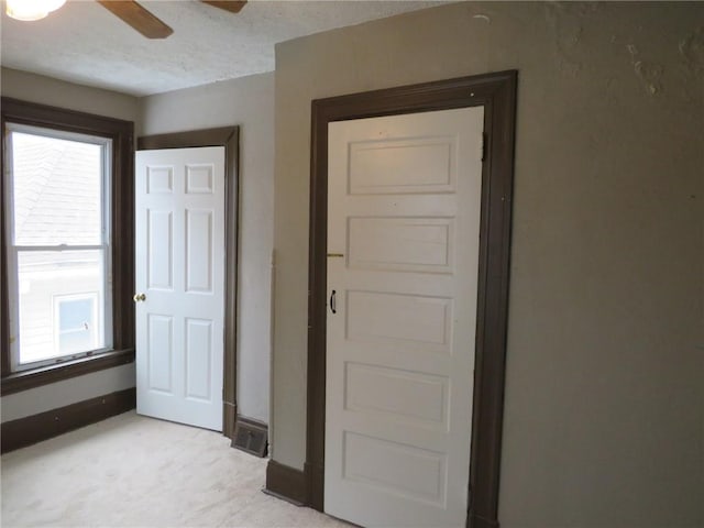 interior space featuring light carpet, a textured ceiling, a ceiling fan, and baseboards