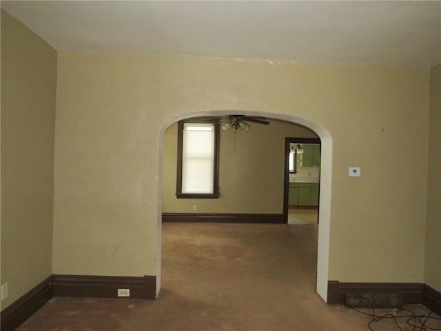 empty room with arched walkways, ceiling fan, and baseboards