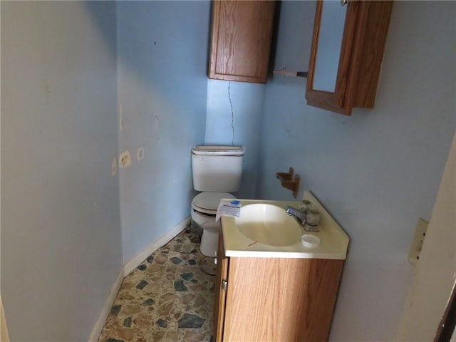 bathroom featuring toilet, stone finish flooring, baseboards, and vanity