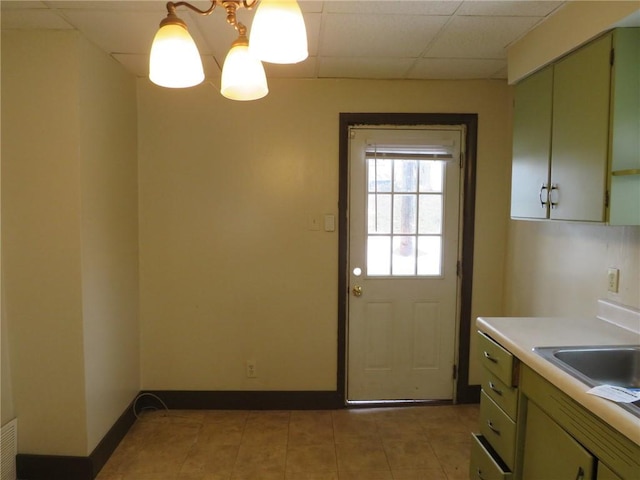 doorway to outside featuring baseboards, an inviting chandelier, a paneled ceiling, a sink, and light tile patterned flooring