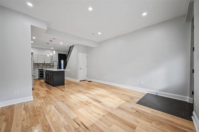 unfurnished living room featuring beverage cooler, sink, and light wood-type flooring