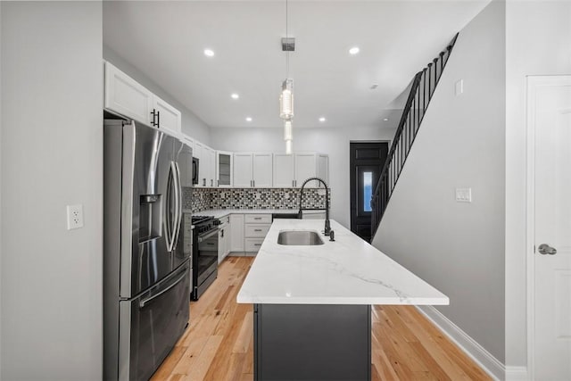 kitchen featuring sink, white cabinetry, stainless steel refrigerator with ice dispenser, gas stove, and a center island with sink