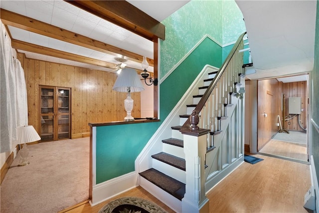 staircase with beam ceiling, hardwood / wood-style flooring, ceiling fan, and wood walls