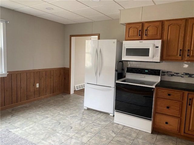 kitchen featuring white appliances, wood walls, a paneled ceiling, and backsplash