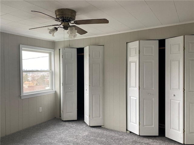 unfurnished bedroom featuring crown molding, carpet floors, two closets, and ceiling fan