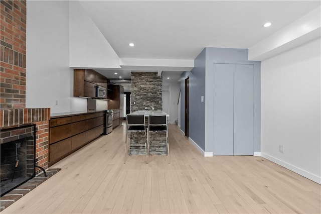 kitchen featuring stainless steel appliances, dark brown cabinetry, a fireplace, and light hardwood / wood-style flooring