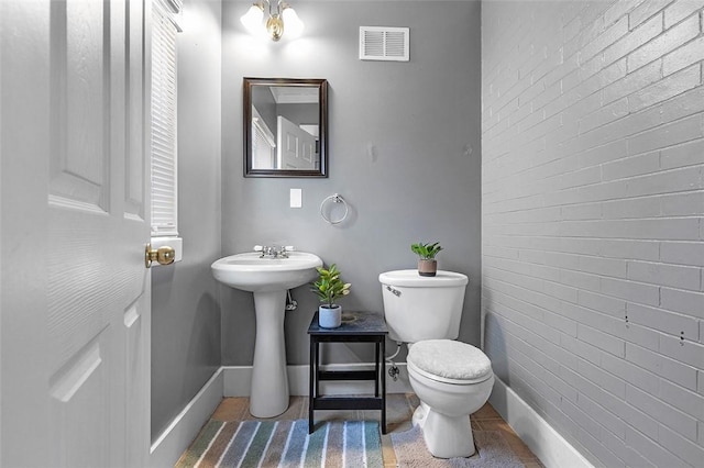 bathroom featuring brick wall, toilet, and sink