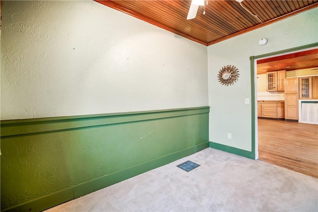 spare room with ornamental molding, light colored carpet, wooden ceiling, and ceiling fan