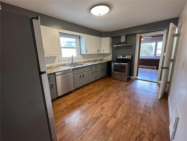 kitchen featuring sink, light wood-type flooring, appliances with stainless steel finishes, decorative backsplash, and wall chimney range hood