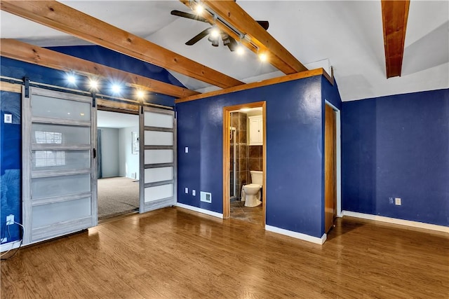 interior space with hardwood / wood-style floors, vaulted ceiling with beams, a barn door, and ceiling fan