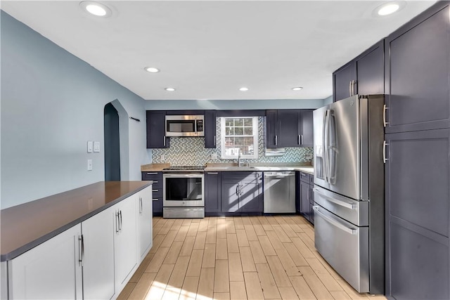 kitchen featuring tasteful backsplash, appliances with stainless steel finishes, sink, and light wood-type flooring