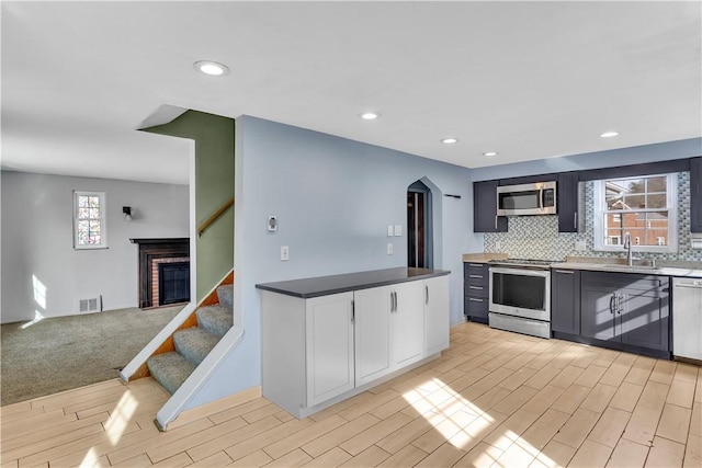 kitchen featuring sink, white cabinetry, light hardwood / wood-style flooring, stainless steel appliances, and backsplash