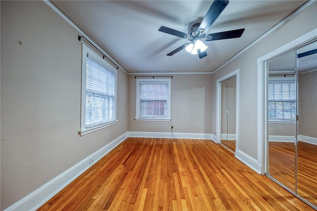 unfurnished bedroom featuring two closets, ornamental molding, multiple windows, and light wood-type flooring