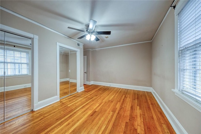 unfurnished bedroom featuring two closets, light hardwood / wood-style flooring, ornamental molding, and ceiling fan