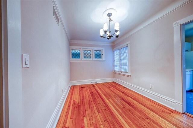 spare room with an inviting chandelier, ornamental molding, and light wood-type flooring