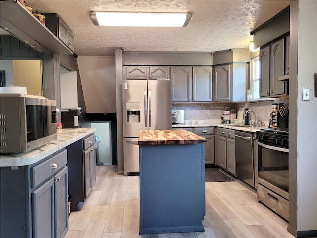 kitchen featuring sink, stainless steel appliances, tasteful backsplash, a kitchen island, and wood counters