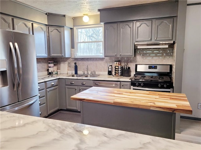 kitchen with sink, backsplash, stainless steel appliances, a textured ceiling, and wood counters