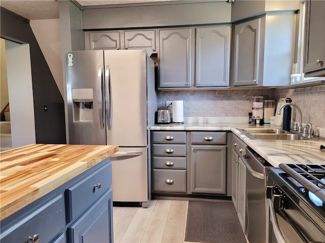 kitchen featuring wood counters, sink, gray cabinetry, stainless steel appliances, and backsplash