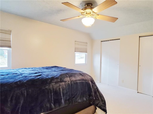 carpeted bedroom featuring multiple closets, lofted ceiling, a textured ceiling, and ceiling fan