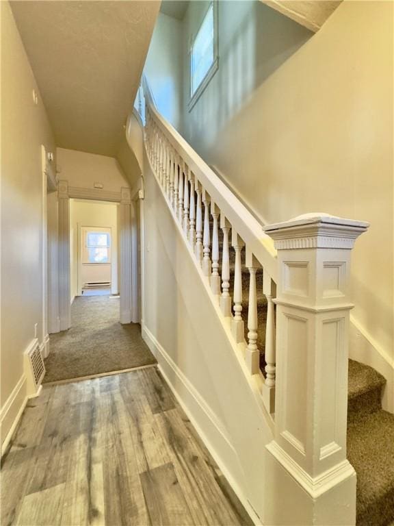 stairway featuring carpet flooring, wood finished floors, visible vents, and baseboards